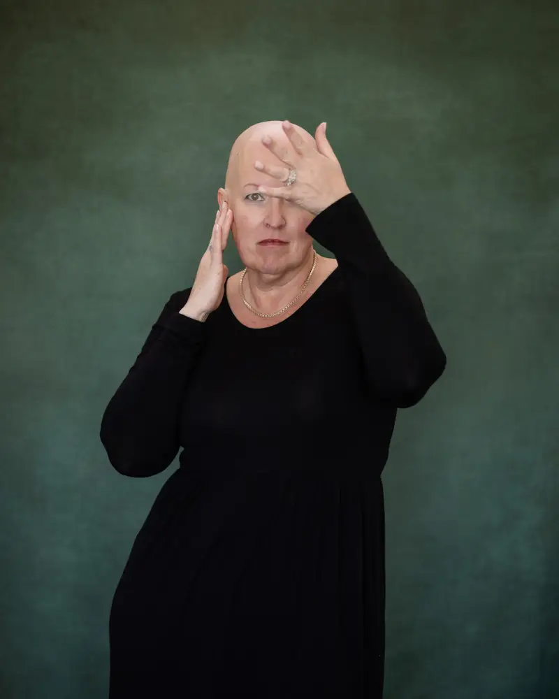 A woman in a long black dress, one hand shading her brow.