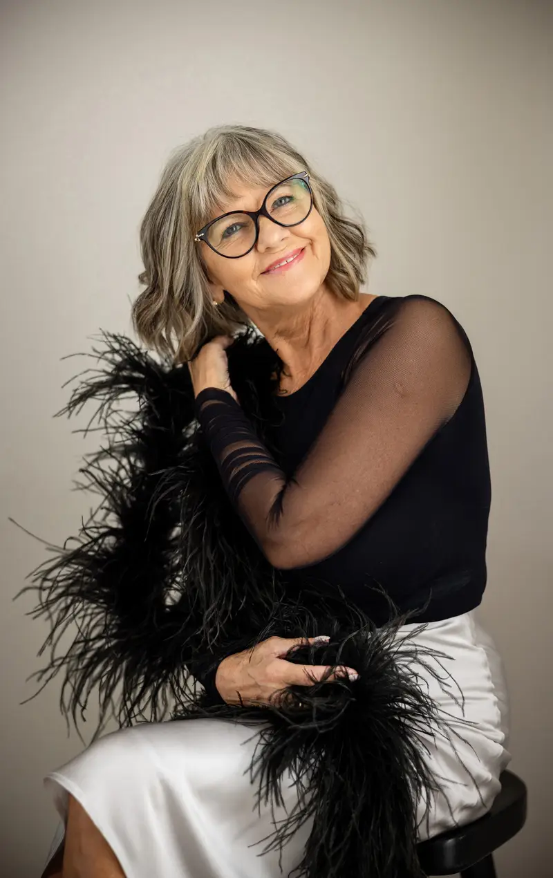 A woman in black with a feather wrap, seated, looking into the lens.