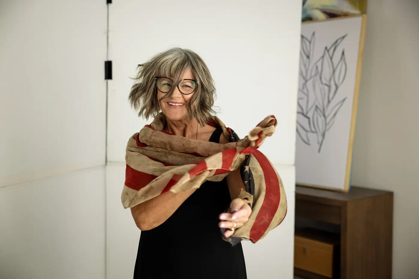 Smiling woman with glasses winding a long patterned scarf around herself