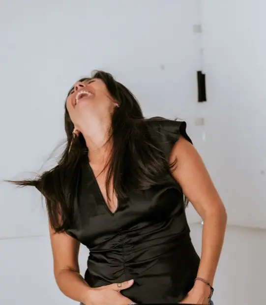 Ivonne Almanza laughing in black clothing against a white wall