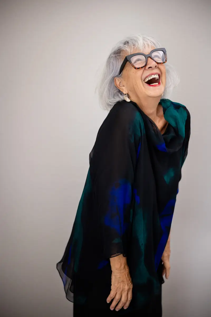 A woman laughing, head tipped back, in a dark patterned scarf.