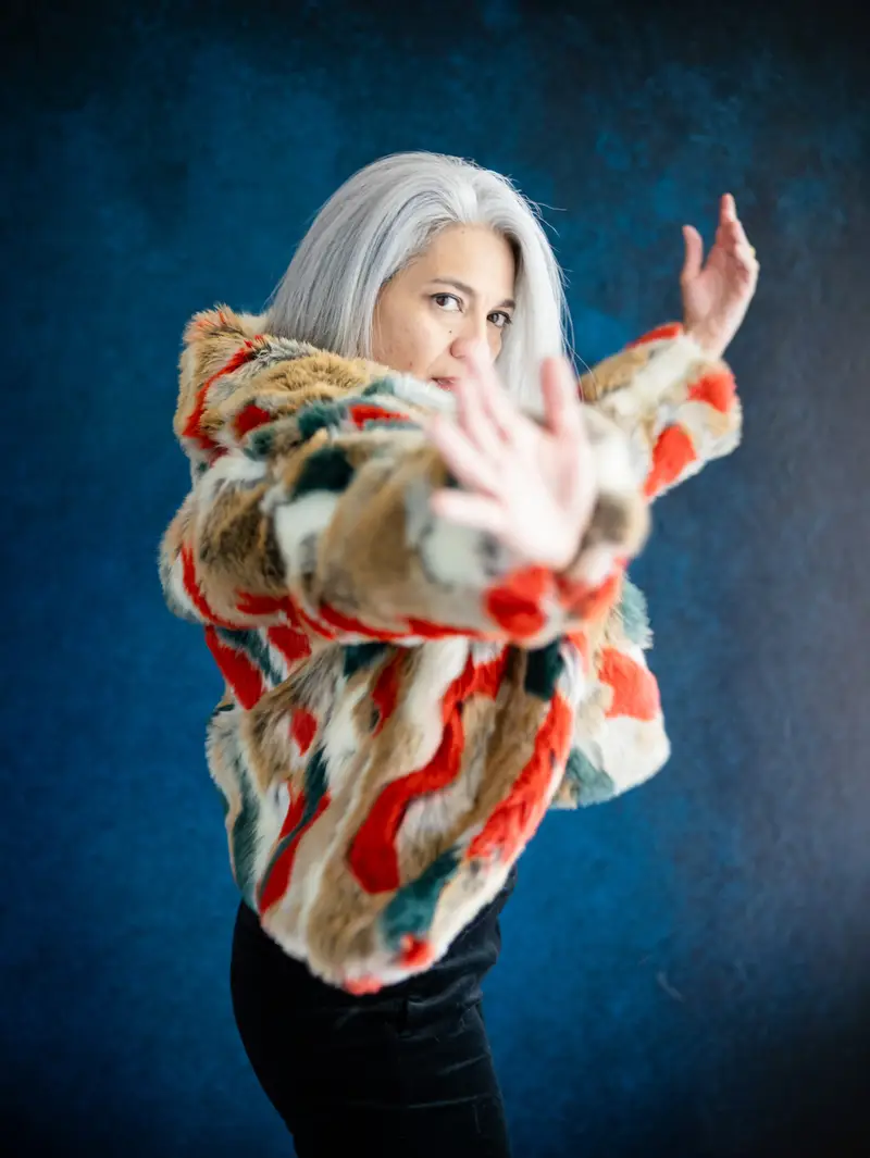 A woman mid-movement, arms open, in a bright patterned coat.